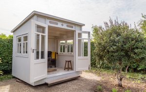 A small white shed for sale in a garden.