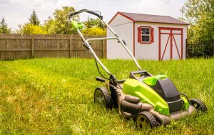 A lawn mower in the grass near a shed store.