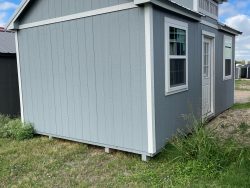 A small gray 12x20 Chalet Shed sitting in a grassy area, available for sheds on sale near me.