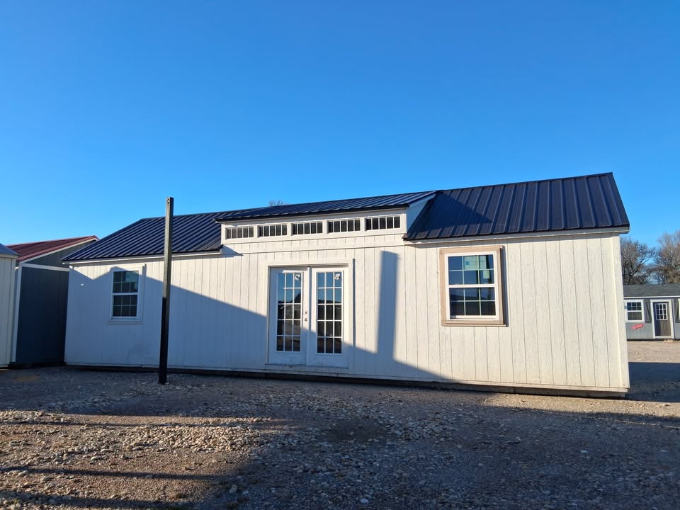  - White modular home with a dark metal roof on a gravel lot under a clear blue sky.