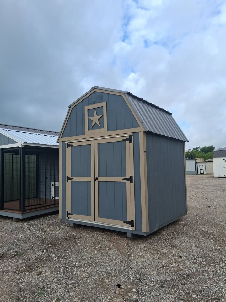  - Blue-gray storage shed with beige trim and a star on the front, siting on a gravel lot.