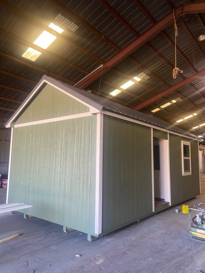  - Prefabricated green modular cabin with white trim and open door inside a large workshop/warehouse area under construction.
