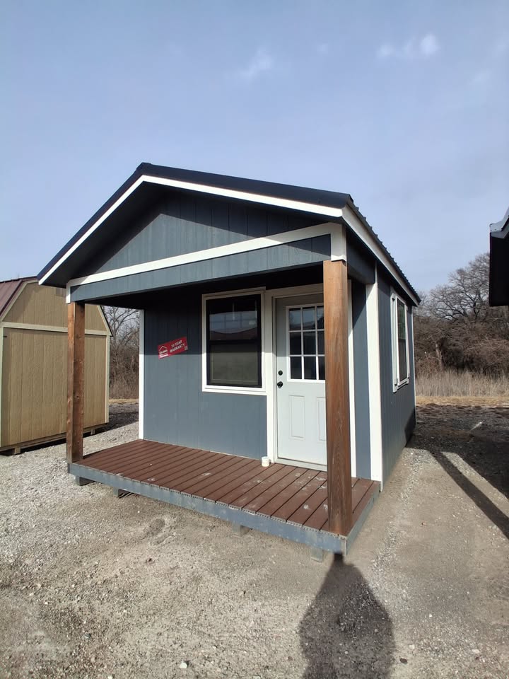  - Small blue-gray shed with a wooden front porch, white door, and trim.