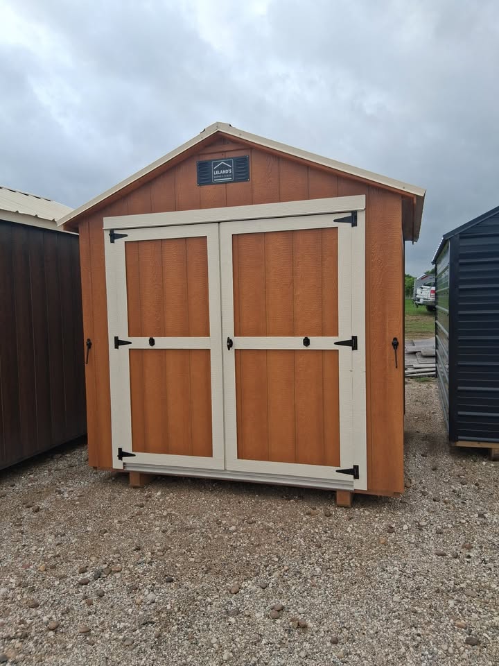  - Wooden shed with double white-trim doors on a gravel lot, cloudy sky overhead.