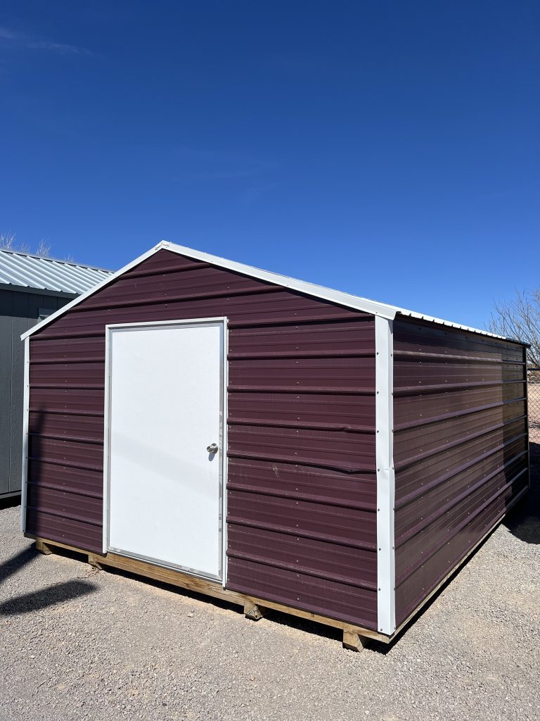  - Maroon metal storage shed with a white door, on a wooden pallet, under a clear blue sky on gravel ground.