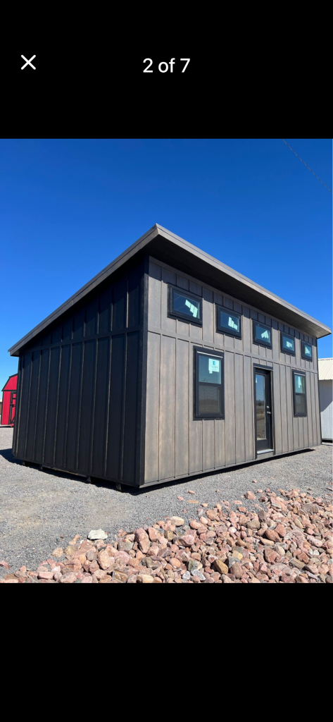  - Dark gray prefab tiny house on a gravel lot under a bright blue sky.
