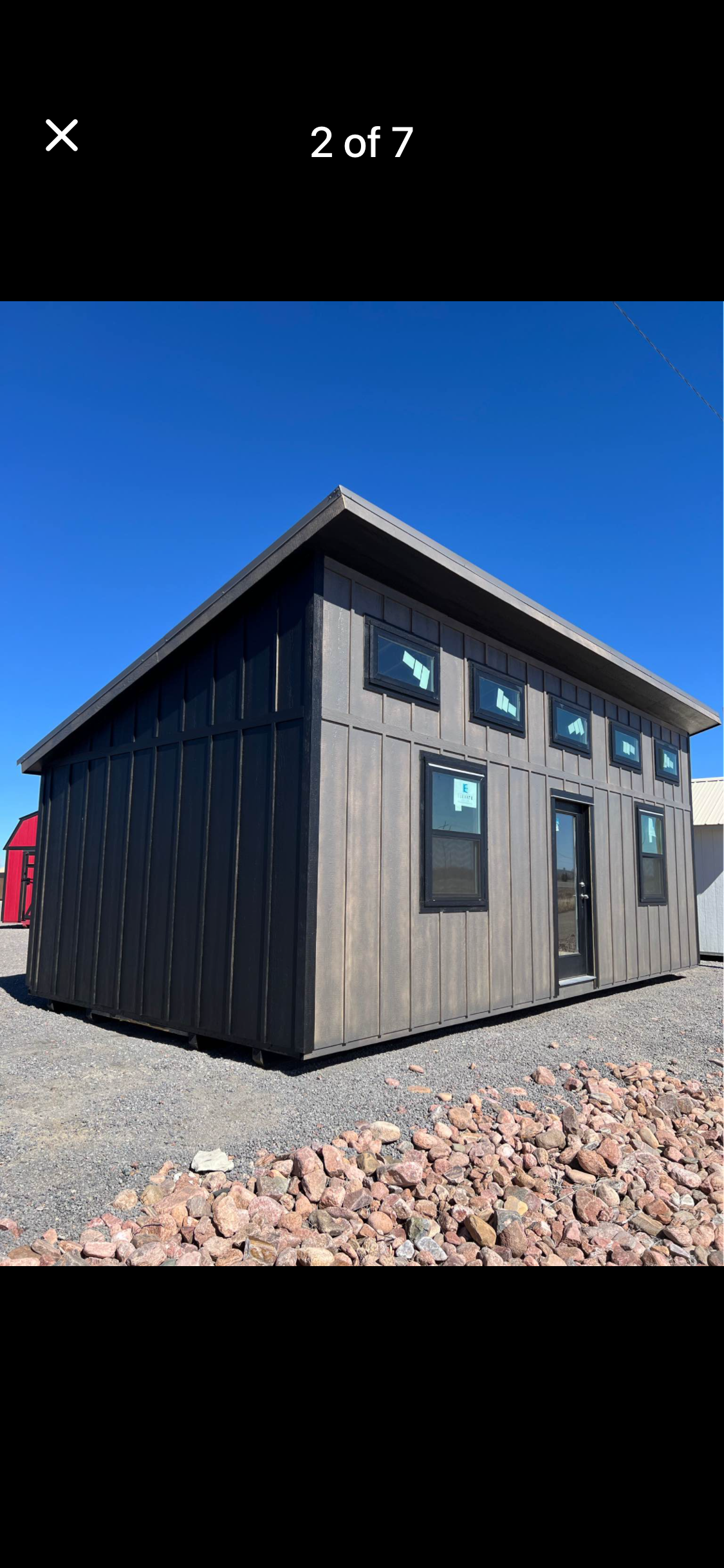  - Dark gray prefab tiny house on a gravel lot under a bright blue sky.