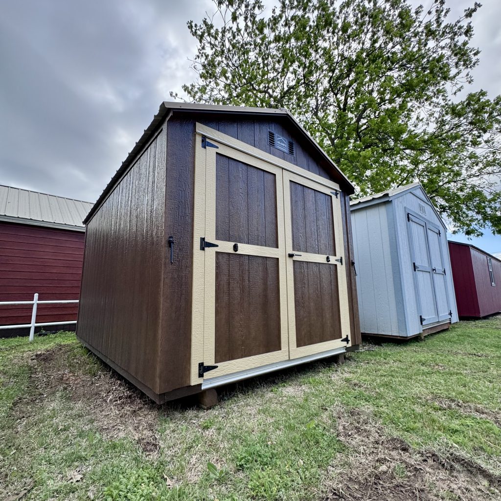  - Row of small wooden storage sheds in brown and beige, with metal roofs, set on grassy ground under a cloudy sky.