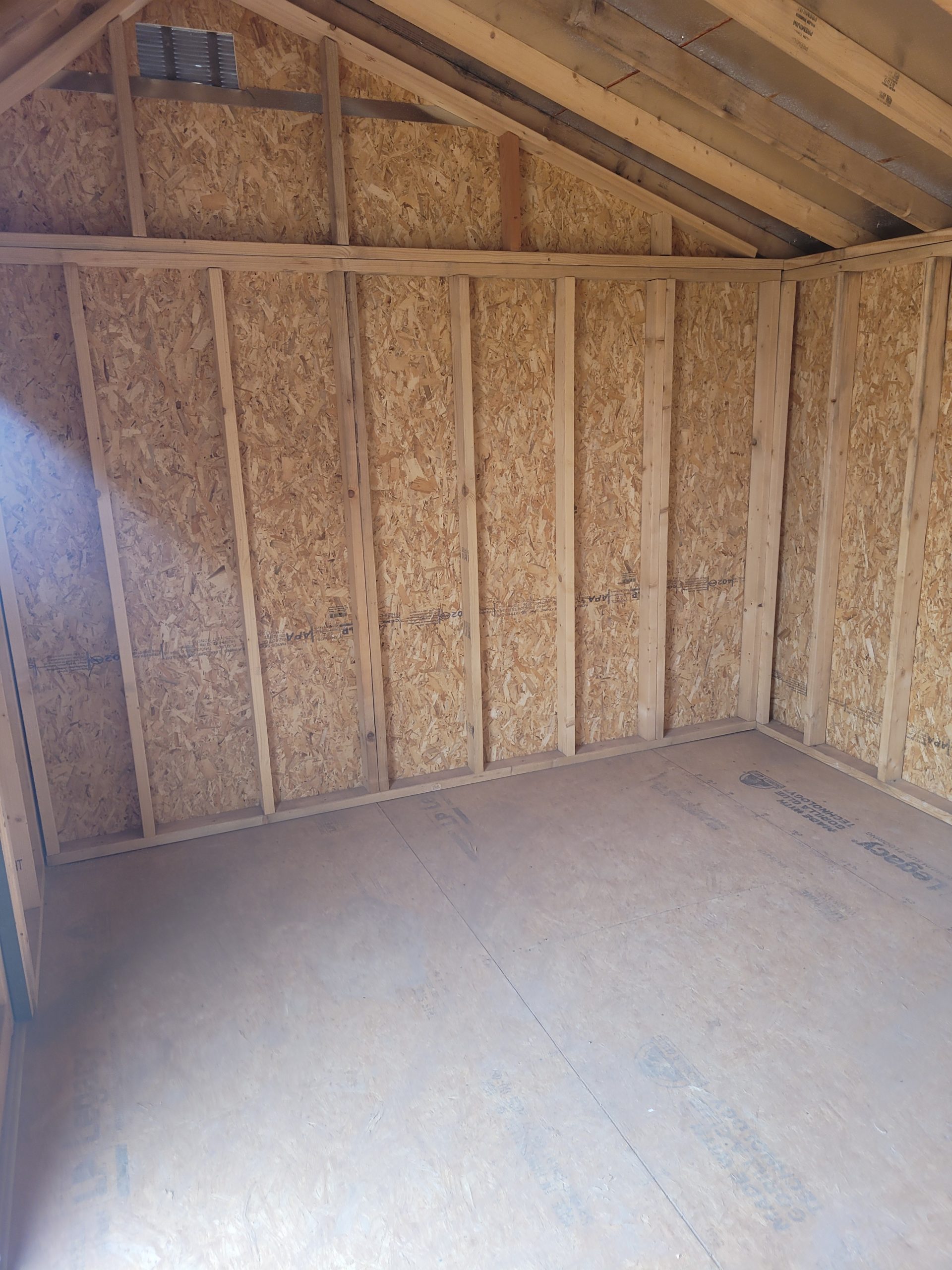 1000012356 - LELAND'S SHEDS - Unfinished interior with exposed wooden studs, oriented strand board walls, and a sloped roof structure under construction