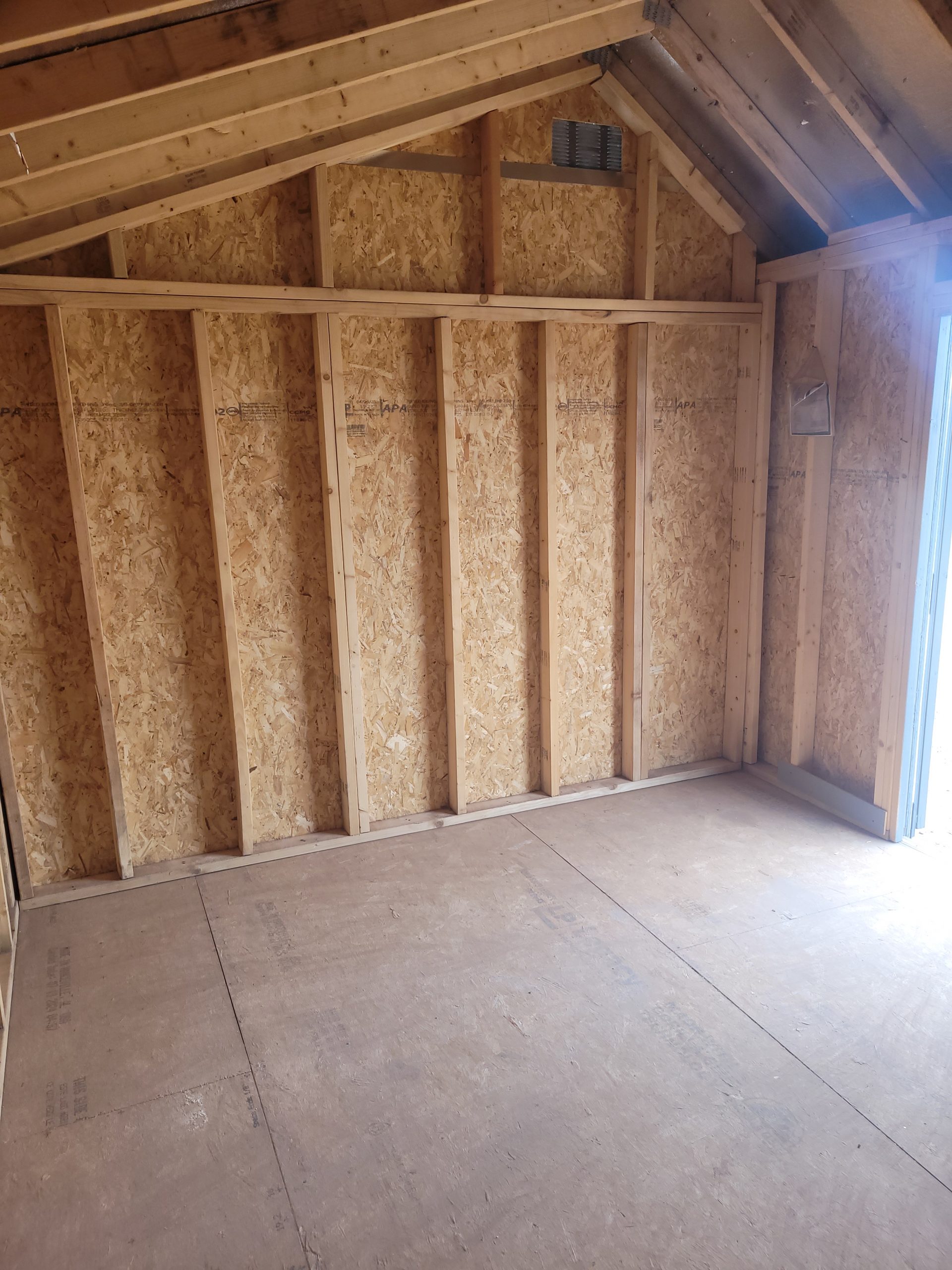 1000012357 - LELAND'S SHEDS - Unfinished interior showing framed walls with vertical studs and OSB sheathing, sloped attic ceiling, and a vent near the top corner of the wall.