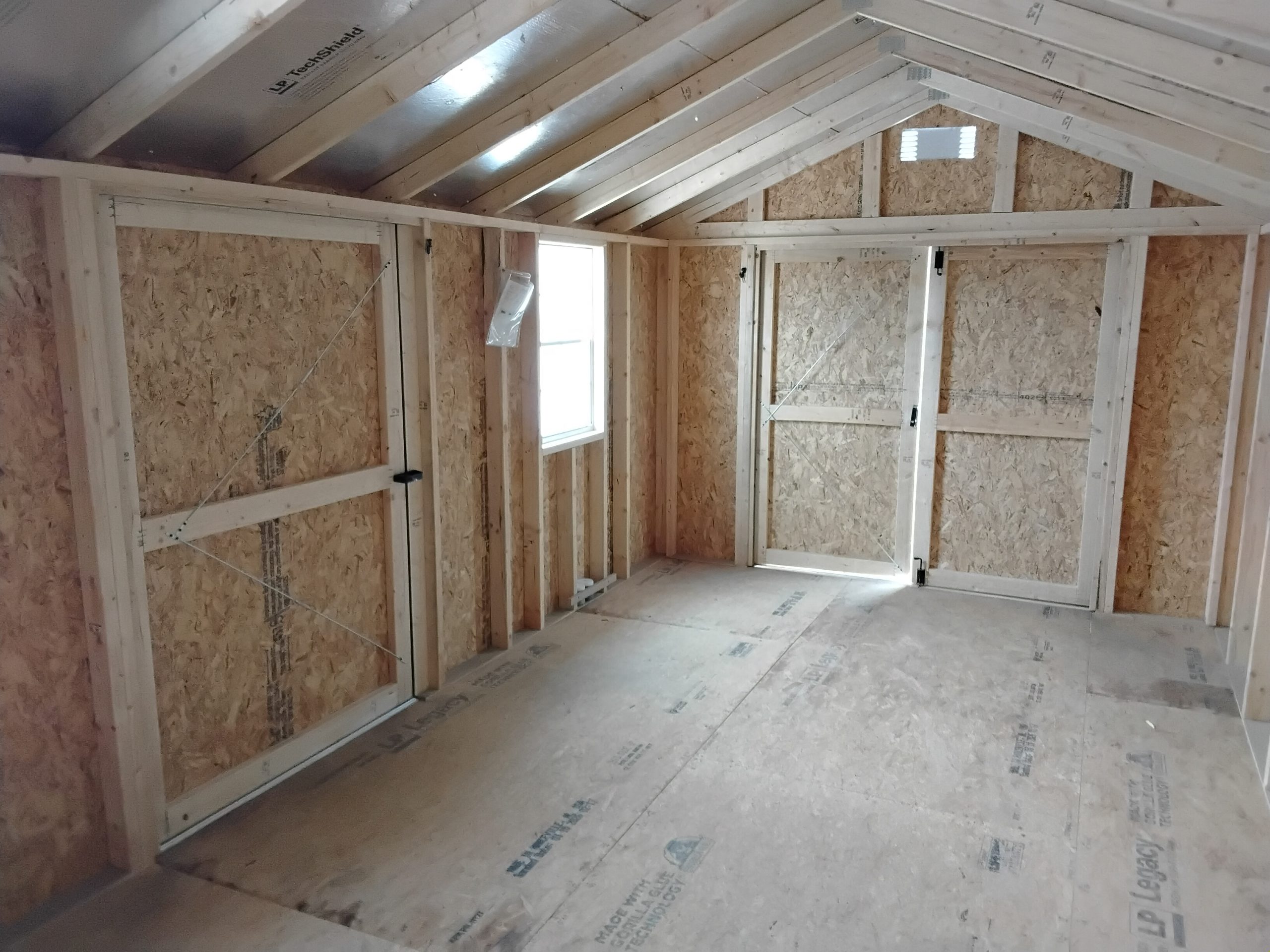 20260505_122820 - LELAND'S SHEDS - Unfinished attic room with exposed wooden studs, OSB walls, and a small window. Sloped roof beams are visible overhead.