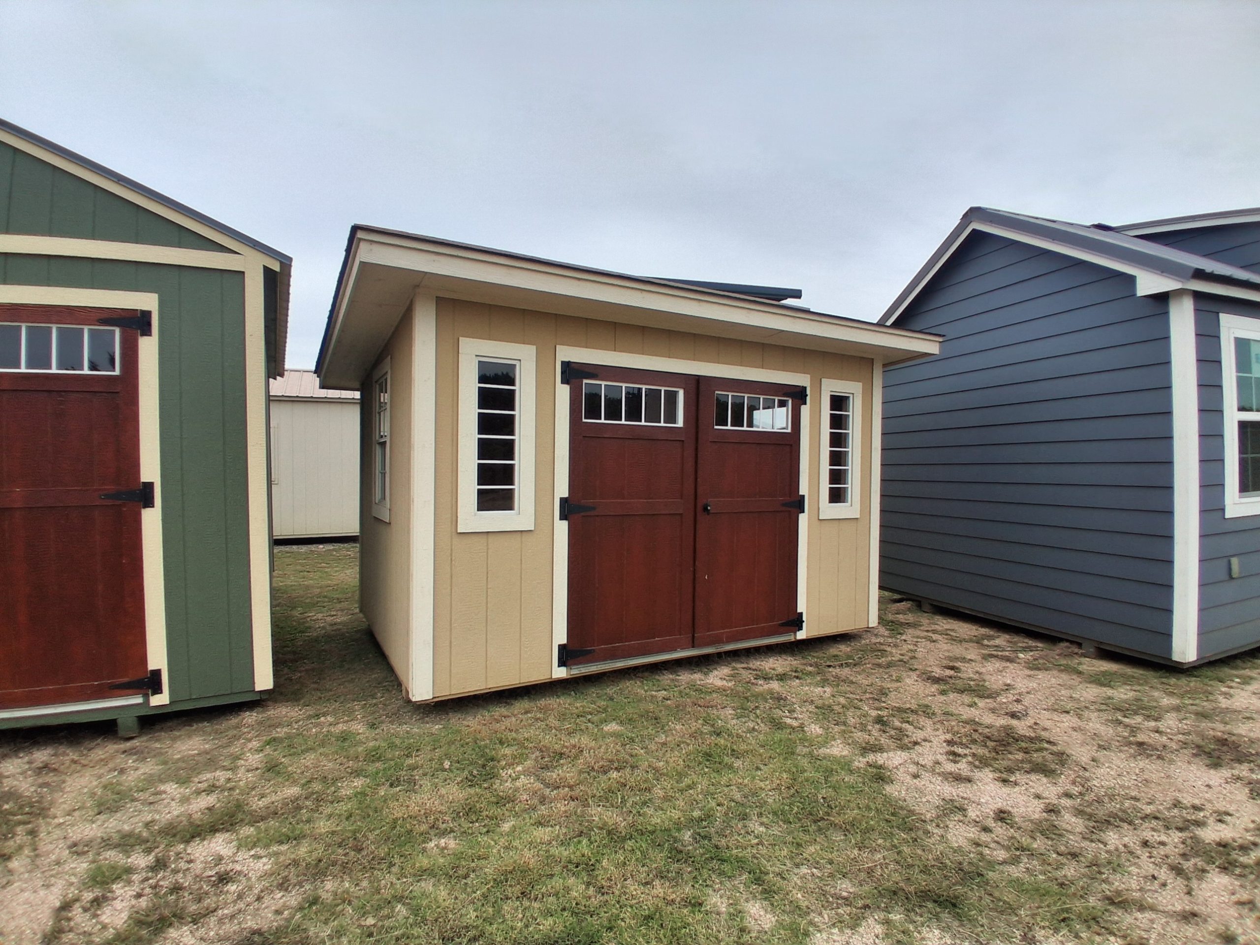 - - Row of small colorful sheds with brown doors and white-framed windows, lined up on grassy ground.
