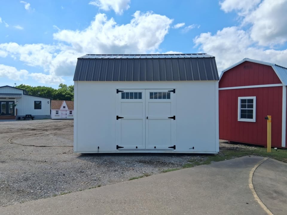  - White storage shed with double doors and black hinges in a gravel yard under a blue sky.