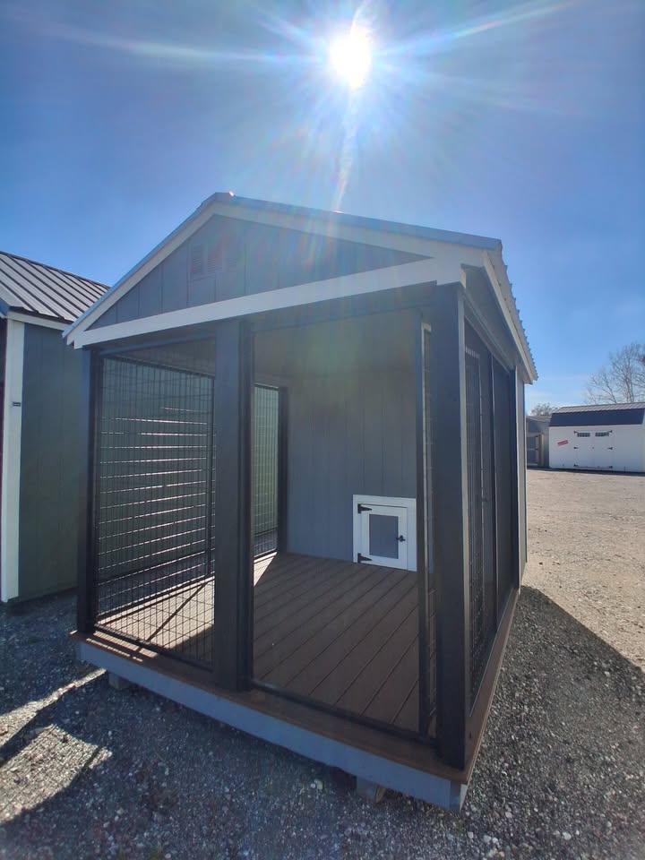  - Sunlit blue-gray shed with a screened-in porch and wooden deck; wire mesh walls and a small pet door cap the enclosure.