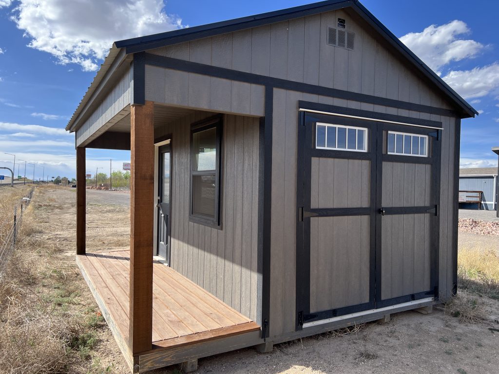  - Small gray shed with dark trim and a wooden front porch in a dry, open landscape under a blue sky.