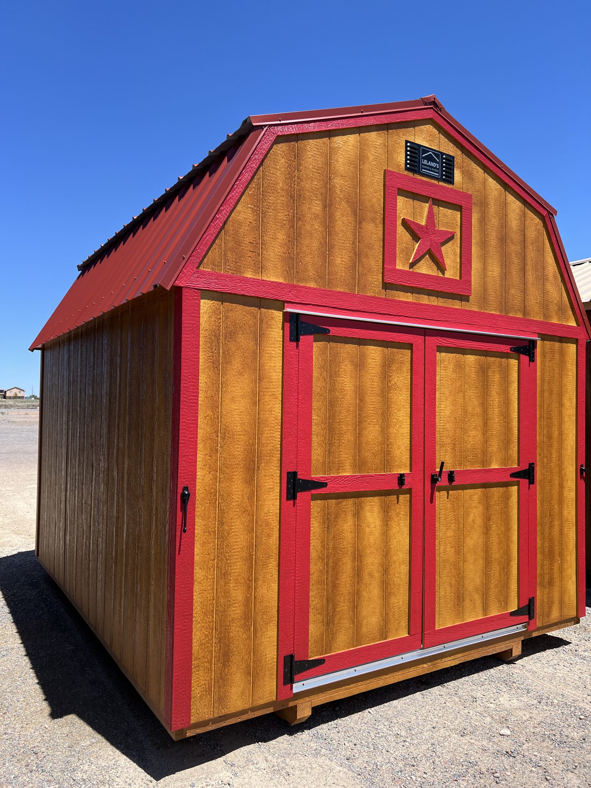  - Barn-style wooden shed with red trim and a red star emblem on the front, under a clear blue sky