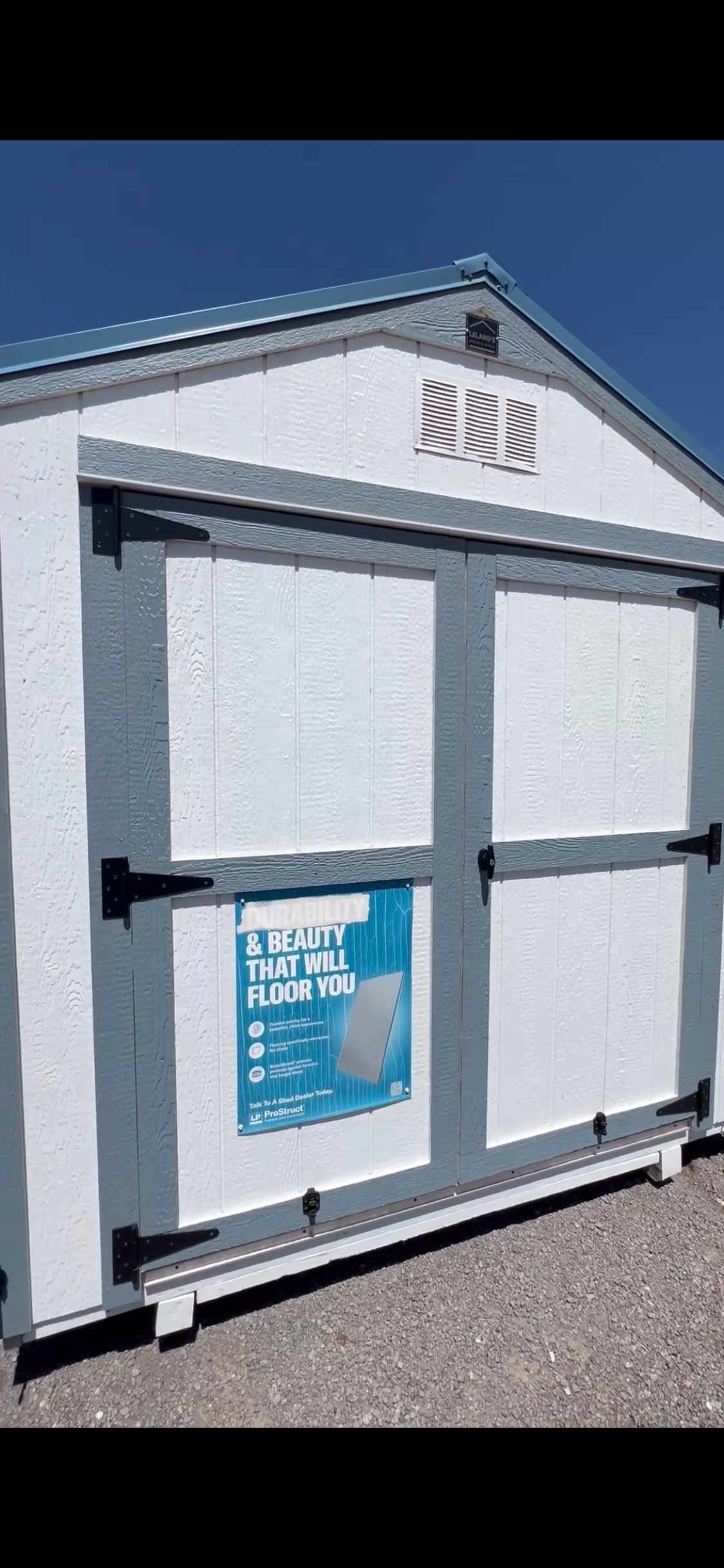  - White shed with blue trim and large sliding doors, a blue advertisement poster on the left door, and a clear blue sky above.