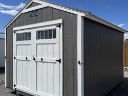 Sheds for Sale - Quality Guaranteed | LELAND'S SHEDS - Sheds for Sale - Quality Guaranteed | LELAND'S SHEDS - Grayscale shed with white-framed double doors on a gravel lot beneath a blue sky with a few clouds