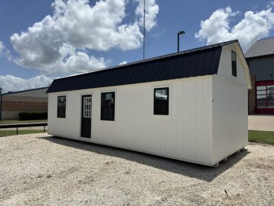 IMG_3856 - LELAND'S SHEDS - White modular building with a black metal roof on a gravel lot under a blue sky with clouds