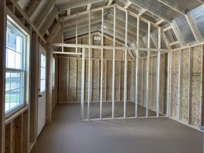 IMG_3858 - LELAND'S SHEDS - Interior of an unfinished house: exposed wooden studs, angled roof framing, OSB walls, and a doorway with windows on the left.