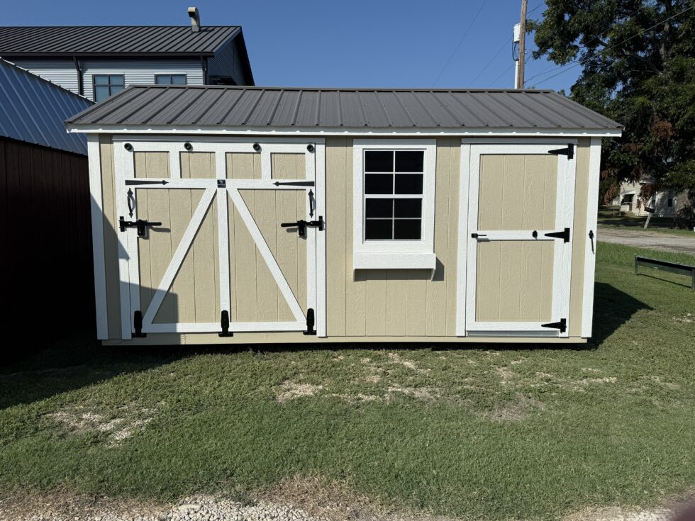 - - Beige shed with white trim and a metal roof, left double barn doors with X bracing and a centered window with a window box on the right side.