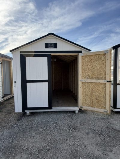 IMG_3870 - LELAND'S SHEDS - White storage shed with black trim on a gravel lot, front doors open showing the dark interior under a blue sky.