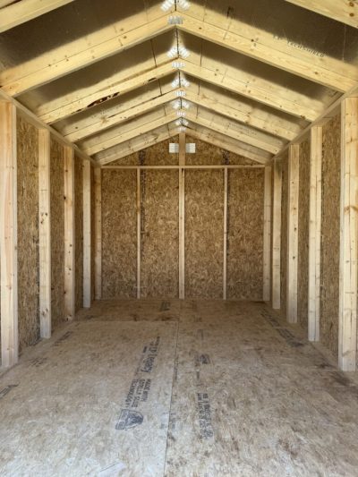 IMG_3872 - LELAND'S SHEDS - Interior of an unfinished wooden shed with exposed studs, OSB walls, and a pitched roof of wooden trusses.”