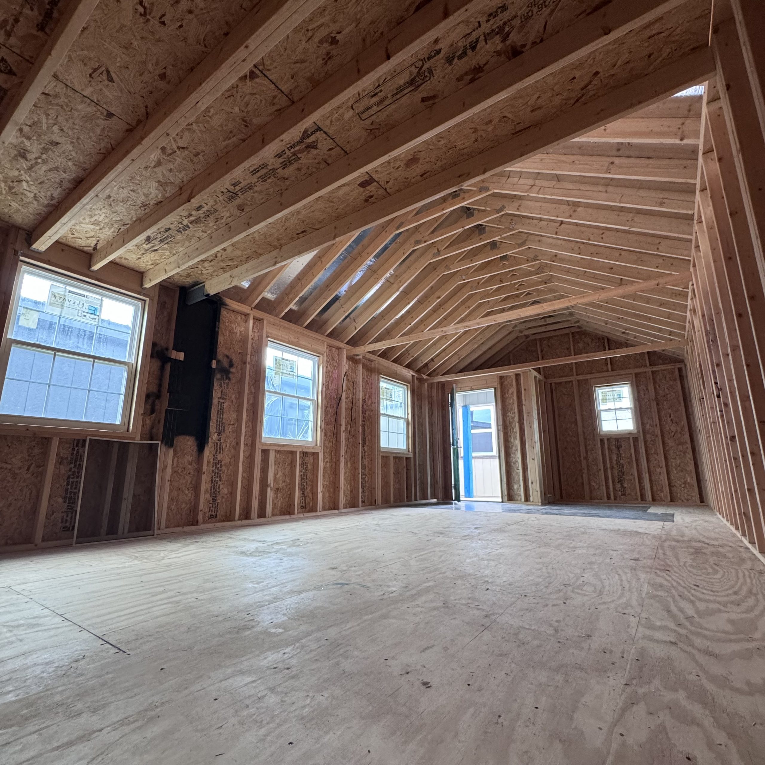 IMG_4068 - LELAND'S SHEDS - Unfinished attic with exposed wooden framing, plywood floors, and multiple windows letting light in