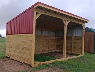  - Open-front wooden storage shelter with a red metal roof, built on a grassy field.