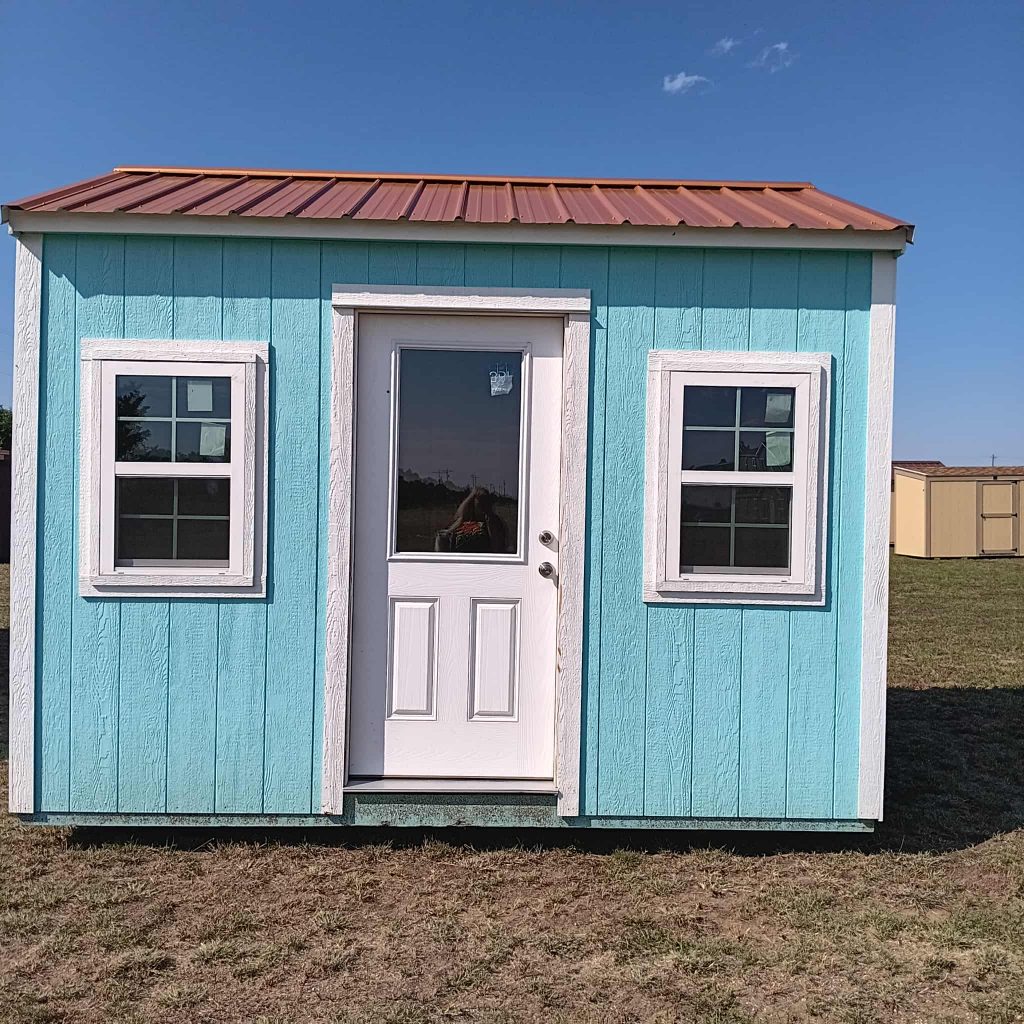  - Front view of a small turquoise shed with white trim, a central door and two windows, under a red roof.