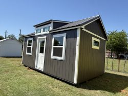 Sheds for Sale - Quality Guaranteed | LELAND'S SHEDS - Sheds for Sale - Quality Guaranteed | LELAND'S SHEDS - Exterior view of a dark-gray shed with white trim and a metal roof on a grassy lawn, with a white shed to the left under a clear blue sky.