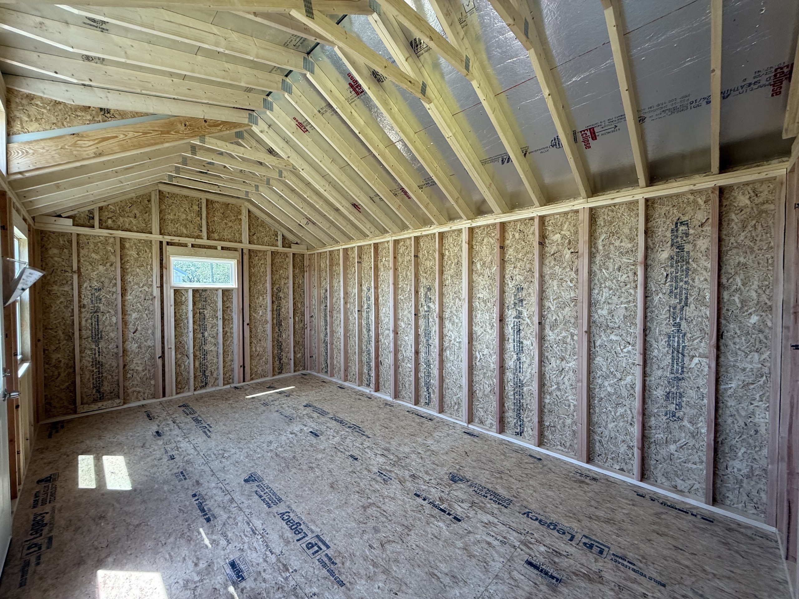 IMG_0232 - LELAND'S SHEDS - Unfinished interior framing: wooden studs line walls with a pitched roof and exposed rafters in progress construction site