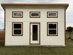 Sheds for Sale - Quality Guaranteed | LELAND'S SHEDS - Sheds for Sale - Quality Guaranteed | LELAND'S SHEDS - Beige prefab house with brown trim, two rows of windows: three small horizontal windows on the upper level and two large windows with a central glass door on the lower level.