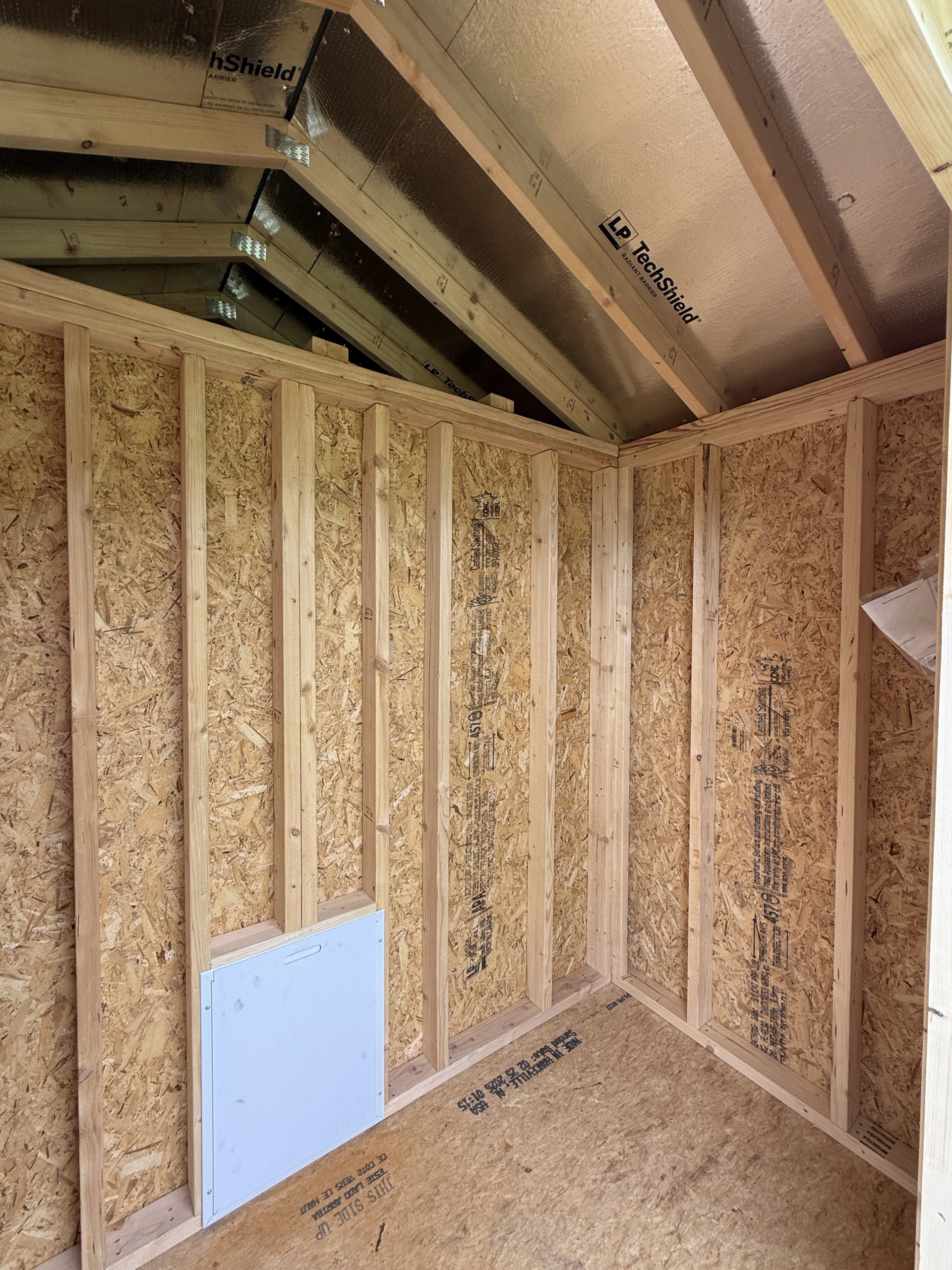 IMG_0853 - LELAND'S SHEDS - Framing of a room under construction with wooden studs, OSB walls, and an exposed ceiling of metal panels labeled TechShield