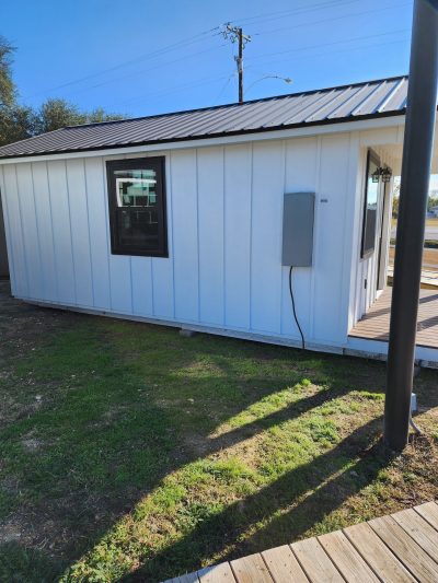 For sale: A small white 12x24 Diamond Cabinette Shed sitting on a grassy area, perfect for those seeking sheds on sale or looking for a shed store near me.
