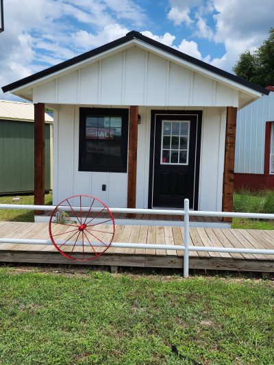 A small white house with a red 12x24 Diamond Cabinette Shed, located near a shed store.