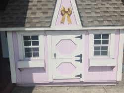 A pink and white 8x8 Victorian Playhouse with a bow on the roof, available at sheds on sale.