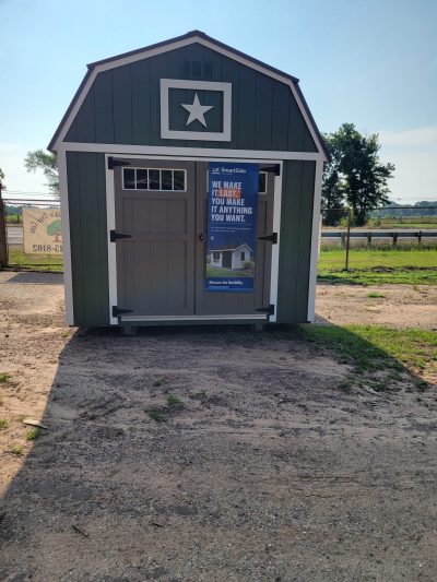 A green 10x18 Lofted Barn with a sign advertising sheds on sale.