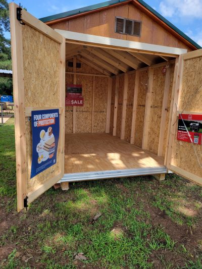 A wooden storage 8x12 Basic Shed with a sign advertising sheds on sale.