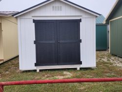 Looking for 10x10 Utility Sheds on sale or a shed store near me? Look no further than this white and black 10x10 Utility Shed sitting on a grassy area.