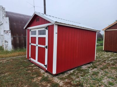 A red and white 10x12 Utility Shed in a grassy area, perfect for storage needs.
