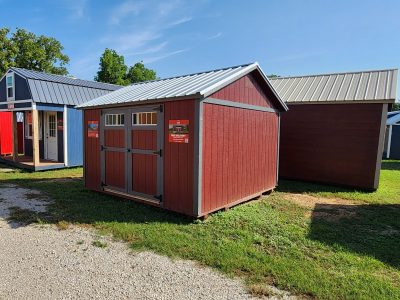 A group of 12x12 Utility Sheds on sale, with some painted in red and blue, parked next to each other.