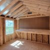 The inside of a 10x12 Utility Shed with wood beams and a window, perfect for storing your belongings or creating an organized workspace.