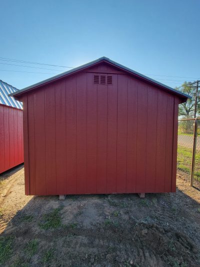 A red 10x12 Basic Shed with a metal roof, available for sale, sitting on a dirt lot.