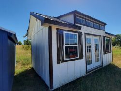 A 12x20 Chalet Shed with a blue roof sitting in a field, available for sheds sale near me.