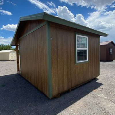 A 12x16 Cottage Shed for sale, sitting in a parking lot.
