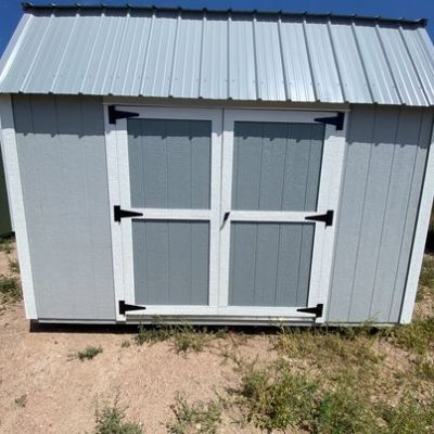 For sale 8x12 Lofted Barn Shed: A gray shed with a metal door in the dirt.