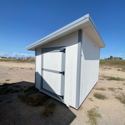 For sale 8x12 Studio Shed: A small shed with a door in the middle of a field, perfect for those looking for 8x12 Studio Sheds on sale near me.
