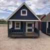 A small blue and white 8x12 Hideout Playhouse in a dirt lot available for sheds sale near me.