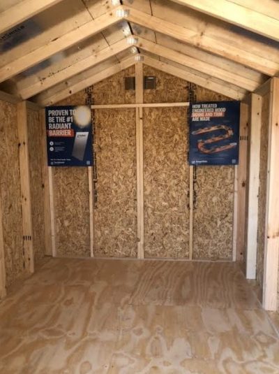 An 8x12 Basic Shed with wood flooring and a sign available for sheds on sale nearby.